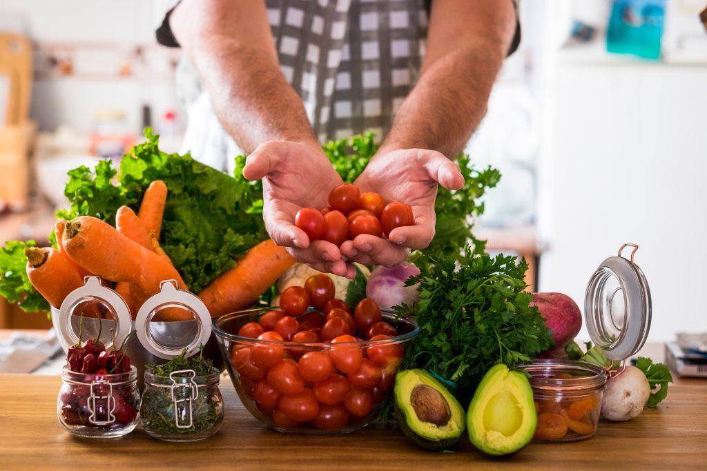 kitchen desk full of vegetables and a person holding tomatoes in their hands